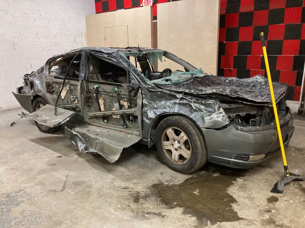 image of a grey car that has been raged on and is in very rough shape with the metal peeling off the sides